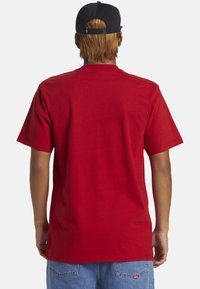 Camiseta roja de manga corta hecha de algodón, con cuello redondo y un corte relajado. La vista posterior muestra un diseño liso sin patrones ni logotipos.