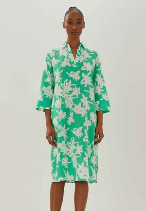 Grünes Kleid aus leichtem Stoff, mit einem weißen Blumenmuster, einem kragenförmigen Ausschnitt und dreiviertellangen Ärmeln.
