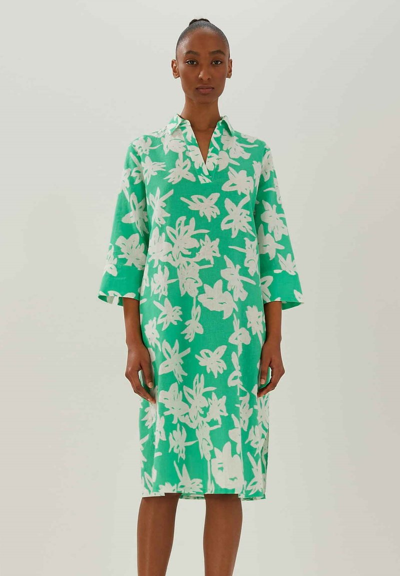 Grünes Kleid aus leichtem Stoff, mit einem weißen Blumenmuster, einem kragenförmigen Ausschnitt und dreiviertellangen Ärmeln.