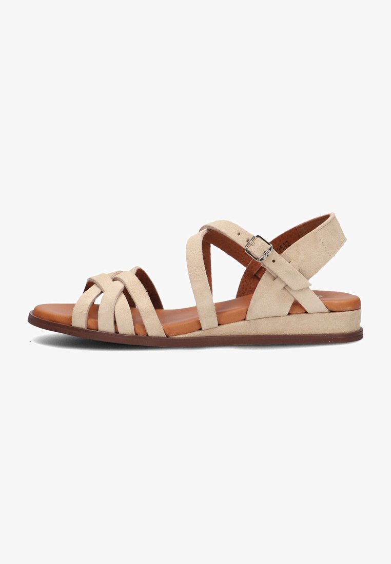 Beige suède sandalen met kruisende banden, enkelband met gesp, platte bruine zool en een gladde textuur.