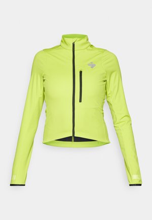 Casaco ajustado de alta visibilidade verde, com mangas longas, gola alta, fecho frontal e um bolso no peito com fecho. Apresenta detalhes em preto.