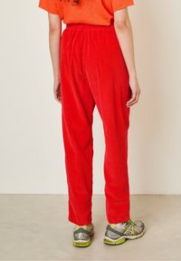 Pantalon en velours côtelé rouge avec une coupe décontractée, présentant des côtes verticales et une taille élastique, associé à des chaussures de sport gris et jaune.