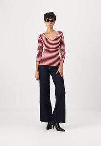 Rot und weiß gestreiftes V-Ausschnitt-Oberteil kombiniert mit dunkelblauen weiten Jeans und schwarzen Knöchelstiefeln, getragen mit Sonnenbrille und Creolen.