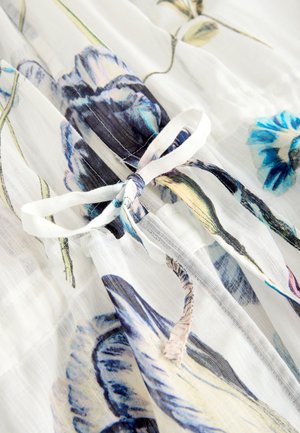 Blommönstrat, genomskinligt tyg med blå och lila blommor på vit bakgrund, knutet med ett mjukt vitt band.