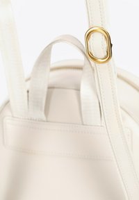 Zaino tondo bianco con una texture in pelle liscia, dotato di un attacco ad anello in metallo dorato e spallacci in tessuto con dettagli di cucitura.