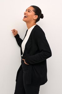 Largo cárdigan negro hecho de material de punto suave, diseño de frente abierto y corte ajustado. Combinado con una blusa blanca y pantalones negros.