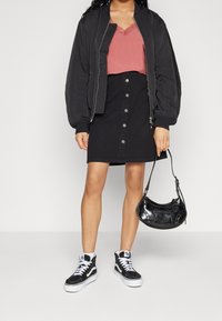 Mustat bombereja, vaaleanpunainen pitsireunainen toppi, mustat napit edessä olevat hameet ja mustat korkeavartiset tennarit, sekä pieni musta käsilaukku.