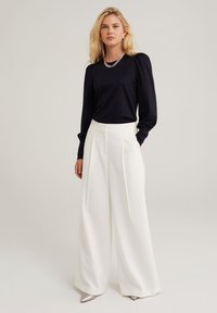 Melna garām piedurknēm tops ar smalku mirdzumu, kombinēts ar baltām plašām biksēm ar augstu jostasvietu un krokām. Sudrabaini vērsti papēži.