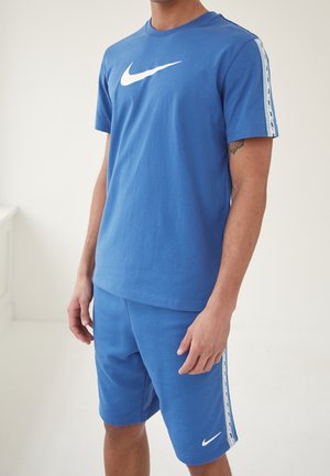 Ensemble de sport Nike bleu comprenant un T-shirt à manches courtes avec un logo blanc et un short assorti, tous deux avec des accents rayés sur les côtés.