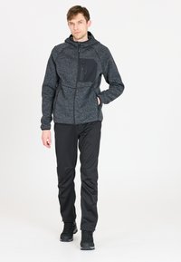 Felpa in pile grigio scuro con tasca anteriore con zip, abbinata a pantaloni neri e calzature nere robuste. Presenta una finitura testurizzata.