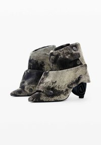 Botines de tobillo texturizados y a rayas en negro y crema, con punta afilada y un diseño de tacón redondeado distintivo que presenta un atrevido detalle circular.