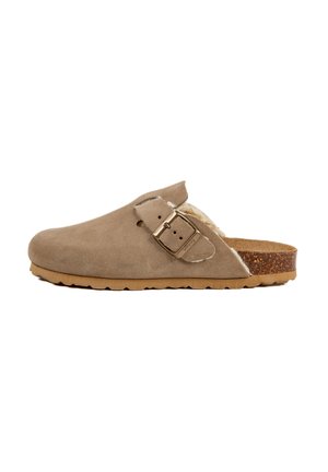 Sabots en daim beige avec une large ouverture, une sangle à boucle en métal et une douce doublure en fourrure. Semelle en liège et semelle en caoutchouc texturé.