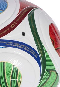 Nogometna lopta veličine 5 u bijeloj boji s crvenim, zelenim, plavim i zlatnim akcentima. Ima teksturiranu površinu i otisnute detalje marke.