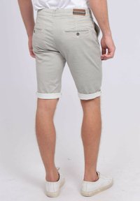 Shorts taillés gris clair avec des ourlets roulés, deux poches arrière avec boutons, associés à des baskets blanches. Tissu texturé.