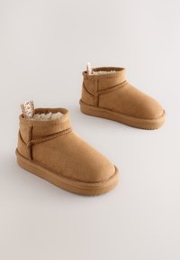 Bottes cheville en daim marron avec une doublure intérieure douce et duveteuse et un petit talon. Couture accentuée et une languette bouclée à l'arrière.