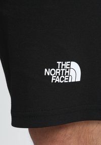 Pantaloni corti neri realizzati in un tessuto morbido, con un logo bianco "The North Face" sull'orlo inferiore, dal design semplice e pulito.
