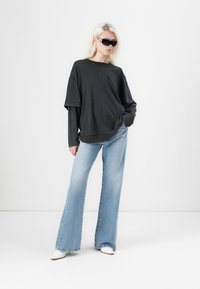 Overmaat zwarte sweatshirt, gelaagd over een lange mouwen top, gecombineerd met lichtblauwe flared jeans en witte hoge hakken. Zonnebril inbegrepen.