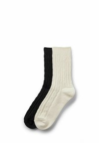 Dwie pary skarpet o prążkowanej fakturze w kolorze czarnym i kremowym. Czarna skarpeta ma fakturowany wzór, natomiast kremowa skarpeta ma gładkie wykończenie.
