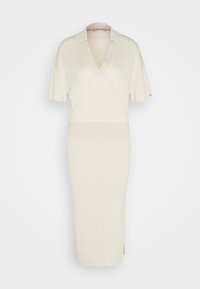Robe tricotée de couleur crème avec des manches courtes et un décolleté en V, présentant une silhouette ajustée et des fentes latérales pour faciliter les mouvements.