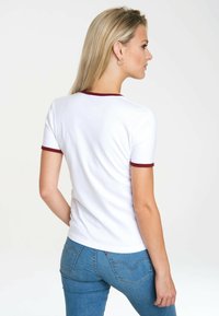 White t-shirt with short sleeves, burgundy trim on collar and sleeves, fitted style, paired with blue denim jeans featuring back pockets.