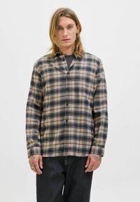 Beige- und schwarze kariert Flanellhemd mit langen Ärmeln, Knopf-Front und lockerer Passform. Das Modell posiert vor einem neutralen Hintergrund.
