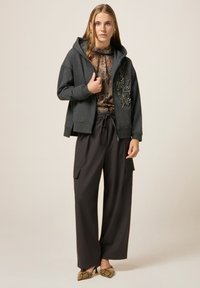 Felpa grigia con zip e abbellimenti decorativi, abbinata a pantaloni larghi scuri e tacchi con motivo. Tessuto morbido e vestibilità rilassata.
