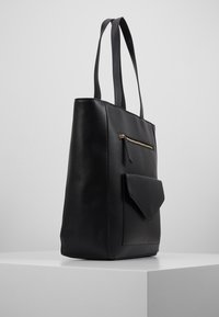 Sac fourre-tout en cuir noir avec deux longues anses, une poche zippée dorée et une poche à rabat sur le devant. Texture lisse, forme rectangulaire.