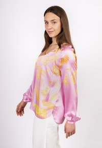 Rosa Satinbluse mit gelben Blumen- und Tiermustern, V-Ausschnitt, langen Puffärmeln und einem leicht abgerundeten Saum.