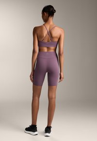 Lila sportos öltözet, amely egy cropped, pántos sportmelltartóból és magas derekú rövidnadrágból áll. Sima anyag, testhezálló fazon. Fekete tornacipők.