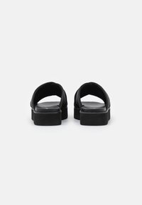 Sandali neri in pelle senza chiusura con una fascia larga, tomaia in pelle liscia e una suola spessa e imbottita. Design semplice senza hardware visibile.