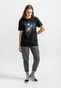 Zwarte katoenen t-shirt met een kleurraf ruimte-thema graphic. Gecombineerd met grijze broeken en zwart-wit geblokte sneakers, wat een casual ensemble creëert.