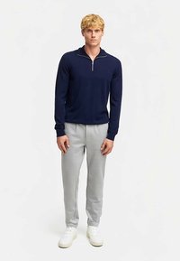 Laivastonsininen vetoketjullinen neule pehmeästä materiaalista, yhdistettynä vaaleanharmaisiin collegehousuihin, joissa sivuraidat, ja valkoisiin tennareihin.