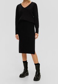 Svart stickad tröja med V-ringning och långärmar, tillsammans med en matchande svart blyertskjol. Stylande med kraftiga svarta ankelskors.