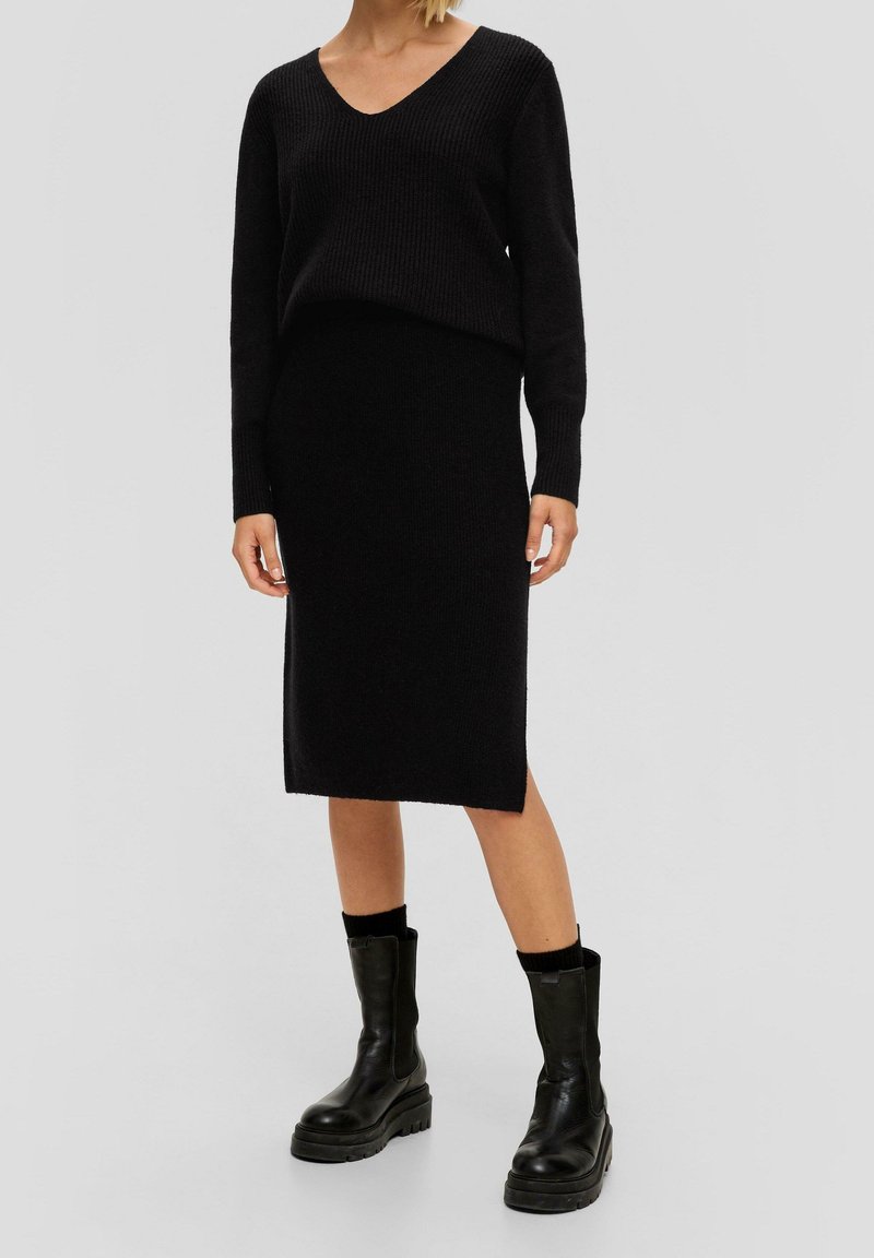 Svart stickad tröja med V-ringning och långärmar, tillsammans med en matchande svart blyertskjol. Stylande med kraftiga svarta ankelskors.