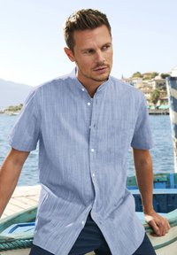 Camicia a maniche corte, con bottoni, in tessuto azzurro chiaro con una delicata texture a righe, dotata di taschino sul petto e colletto alla francese.