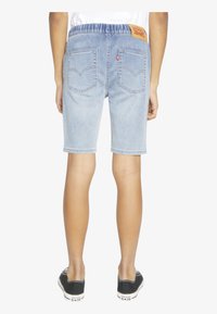 Shorts de mezclilla azul claro con una cintura elástica, que cuentan con dos bolsillos traseros y una etiqueta de cuero con la marca en la cintura.