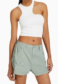 Bílý žebrovaný crop top s asymetrickým výstřihem, doplněný světle zelenými cargo šortkami s bočními kapsami a knoflíkovými detaily.