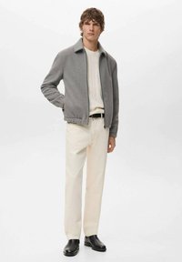 Giacca in pile grigia con colletto, zip frontale e vita elastica, abbinata a pantaloni color crema e scarpe nere, su sfondo bianco.