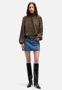 Braune Bluse mit Leopardenmuster und Ballonärmeln, kombiniert mit einem Jeans-Minirock, schwarzen kniehohen Lederstiefeln und einem schwarzen Gürtel.