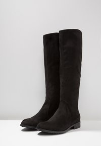 Czarne zamszowe botki do kolan o gładkiej fakturze, zaokrąglonym nosku, niskim obcasie i bez widocznych elementów metalowych lub ozdób.