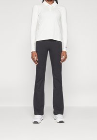 Biała polo z długim rękawem z zapięciem na guziki, w połączeniu z czarnymi dopasowanymi spodniami. Model nosi białe buty sportowe. Prosty, casualowy strój.