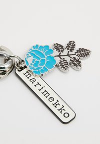 Fém kulcstartó, kék virágmintával és fekete levéllel. Egy téglalap alakú címke kíséri, melyen fehér alapszínű "marimekko" felirat található.