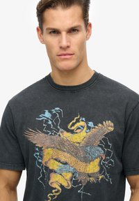 T-shirt en coton noir avec un graphique d'aigle coloré et le texte "Superdry", coupe décontractée et col rond.