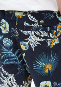Pantaloni corti floreali blu navy con una stampa vivace di fiori gialli e acquamarina, una tasca posteriore e un'etichetta con il logo Vans. Materiale morbido.