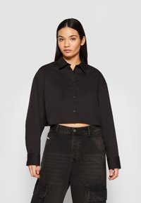 Black cropped long-sleeve shirt with a collar and button closure, paired with high-waisted black cargo pants featuring pockets.