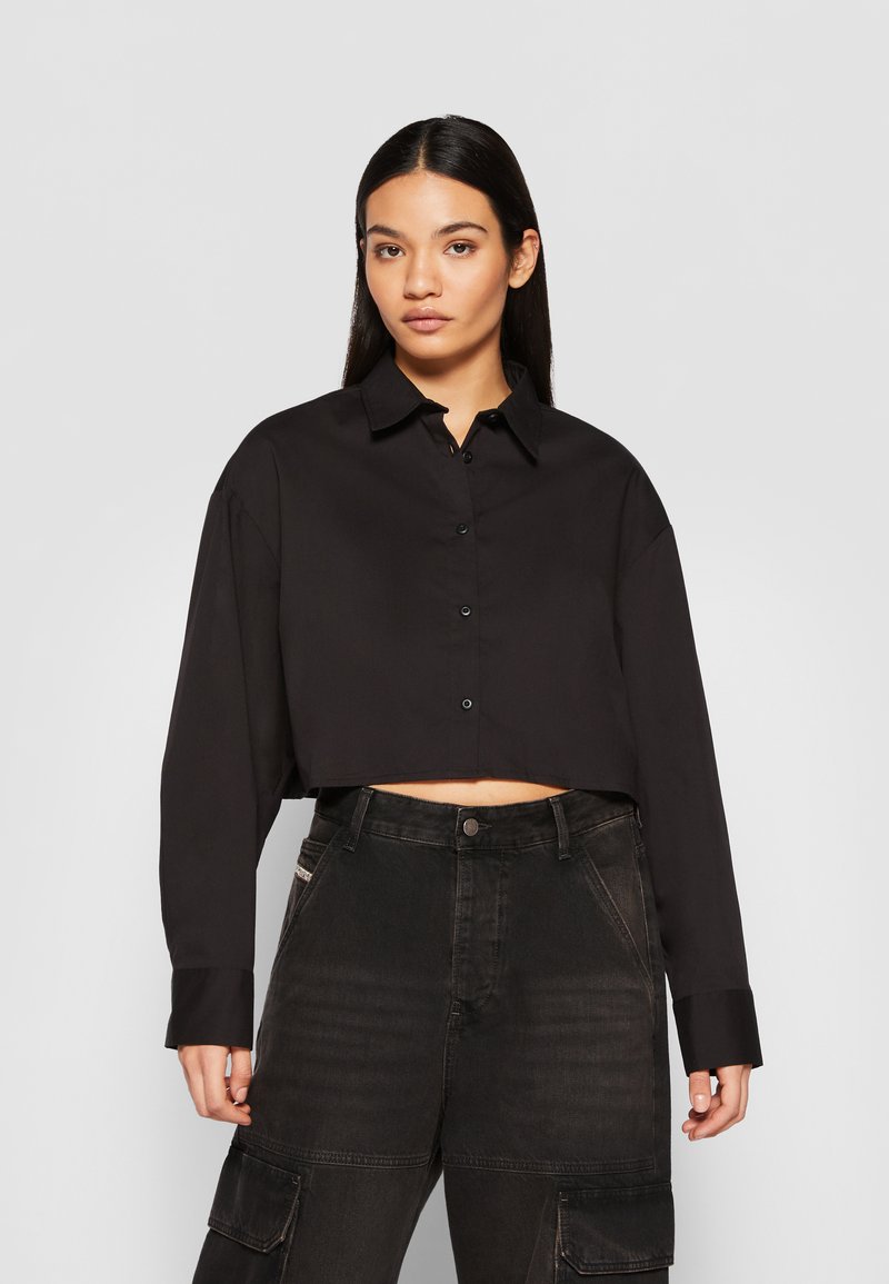 Black cropped long-sleeve shirt with a collar and button closure, paired with high-waisted black cargo pants featuring pockets.