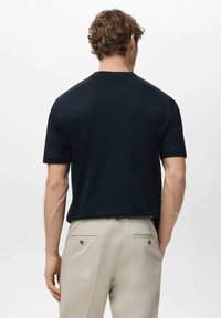 Granatowy, krótkorękawowy sweter z dzianiny z okrągłym dekoltem, luźnym krojem i subtelną fakturą. W połączeniu z jasnobeżowymi spodniami.