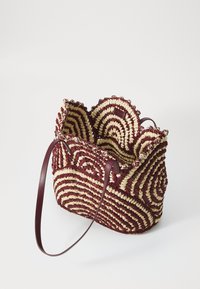 Υφασμένη τσάντα από άχυρο σε μπορντό και μπεζ με σπειροειδές μοτίβο, διαθέτοντας ένα φούσκωμα στην άκρη και μια μακριά, λεία δερμάτινη λωρίδα.
