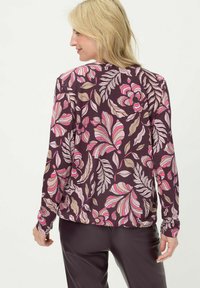 Rückansicht eines langärmligen Oberteils mit dunkelviolettem Hintergrund und großen Blumenmustern in Pink, Creme und Beige, mit lockerem Schnitt.