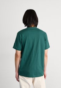 Green cotton t-shirt with short sleeves, crew neck, and contrasting trim along the shoulders. Smooth texture, relaxed fit, minimalistic design.